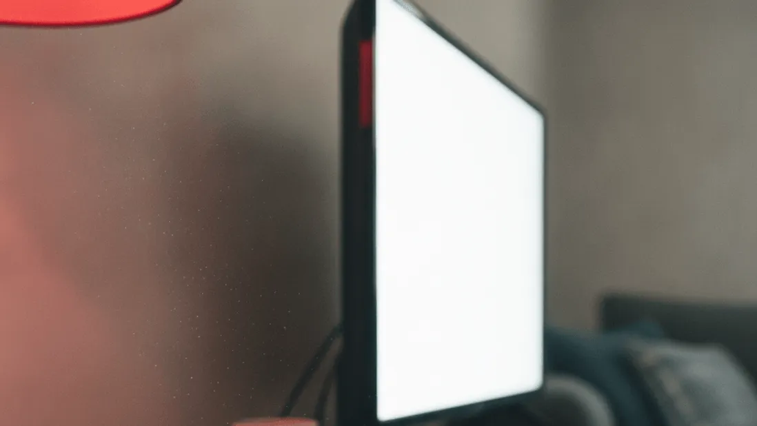 A hand holding a remote control near a router with lit indicators on a low shelf, in afternoon light.