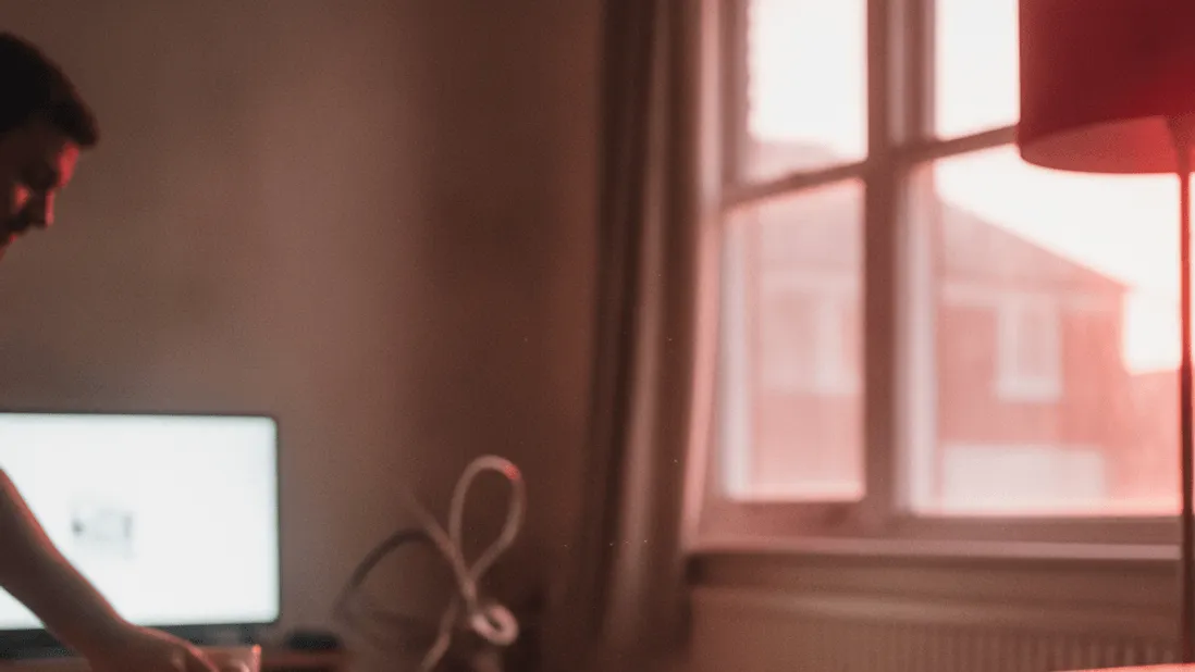 A documentary-style shot of a broadband router on a wooden shelf in a living room, with a man in the background.
